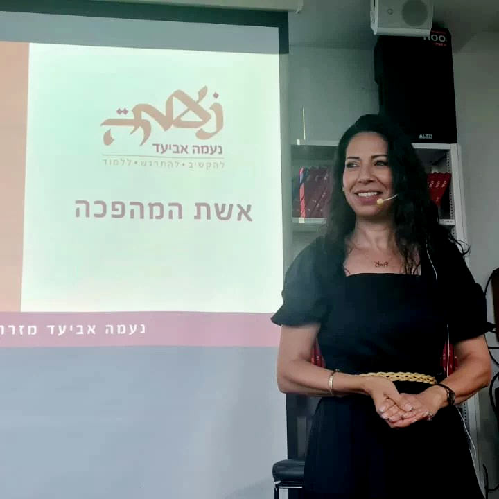 נעמה אביעד בסדנה "אשת המהפכה" ברקע מוקרנת שקופית עם הלוגו של נעמה ושם הסדנה